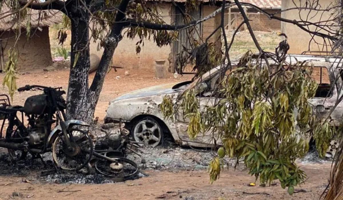 A burnt out motor cycle and car stand amid charred debris in a dusty compound.