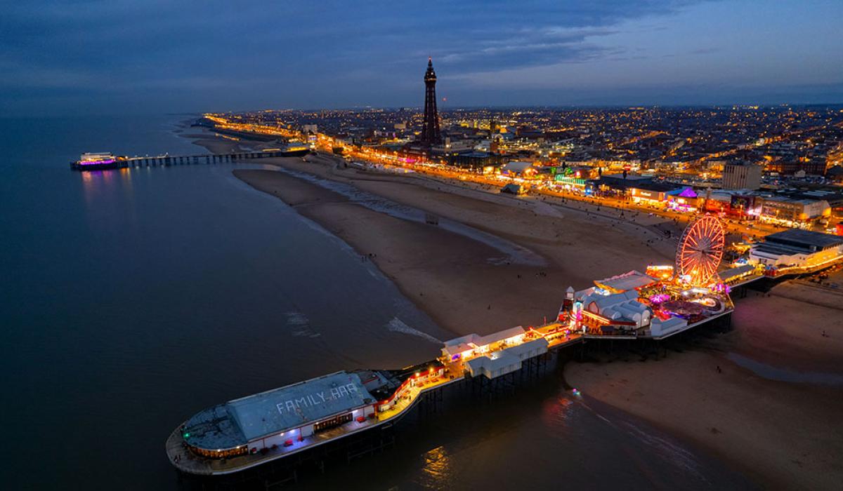 An aerial view at dusk of a brightly lit pier and promenade of the seaside town of Blackpool