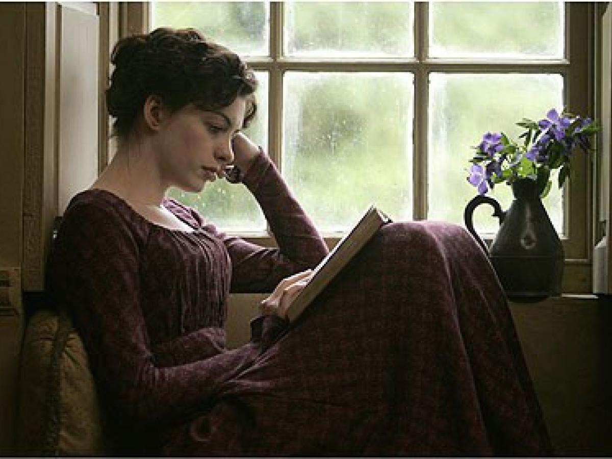 A woman in 18th century clothes sits within a windowsill reading a book