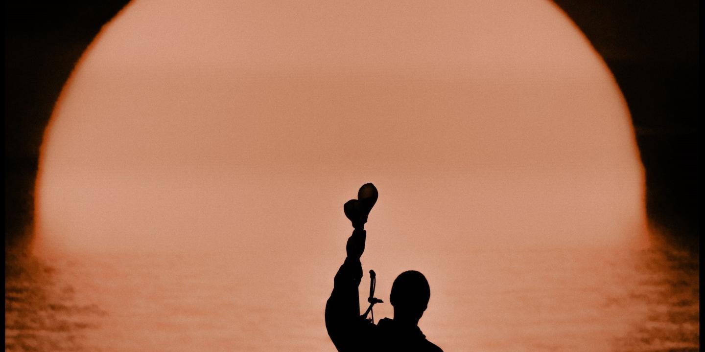 A silhouette of a musician holding up shakers.