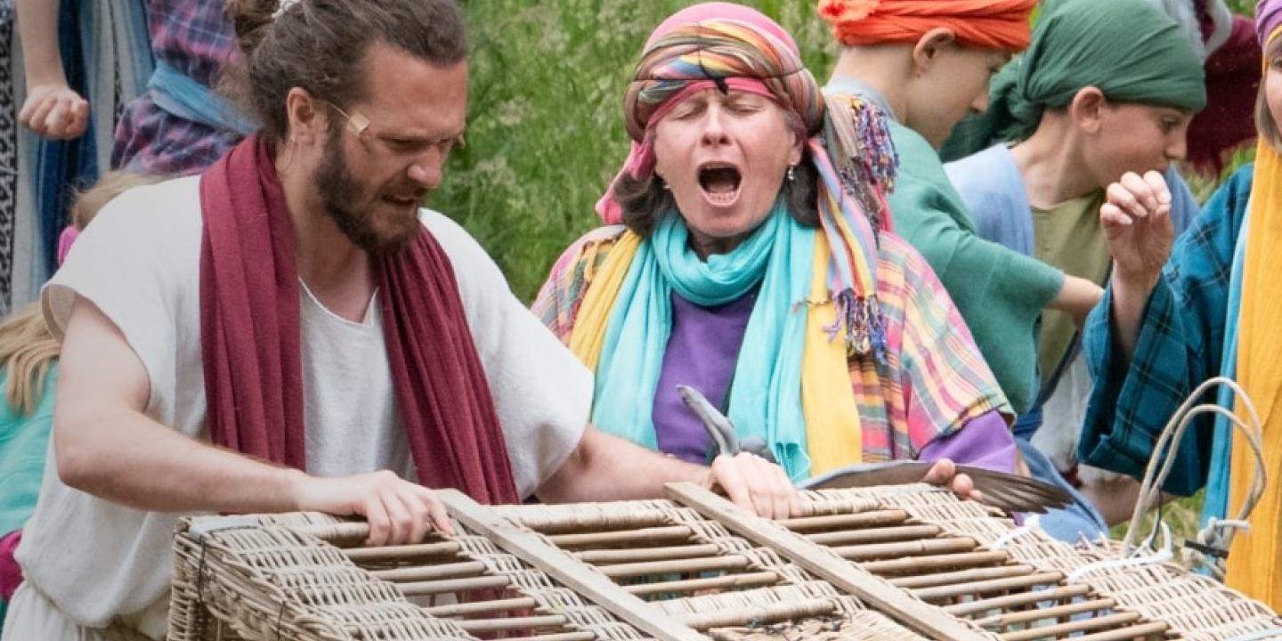 An outdoor theatrical setting shows Jesus with a basket.