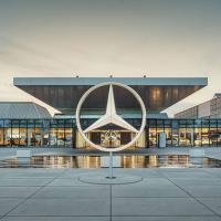 A large sculpture of the Mercedes Benz three-point star stands in front of a large, low glass fronted showroom.