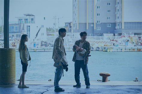 Three people, one carrying a baby, stand on a dock side at a harbour