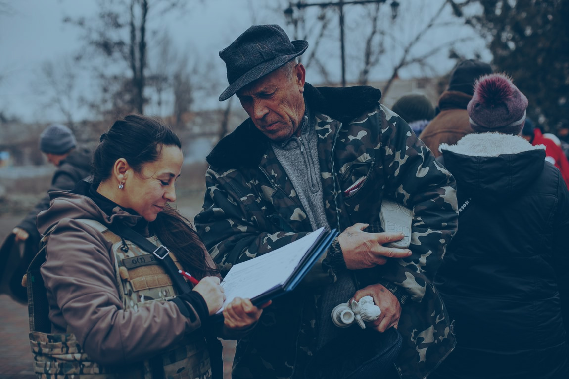 An aid worker and a local resident consult a list as they stand outside in a battle-affected town.