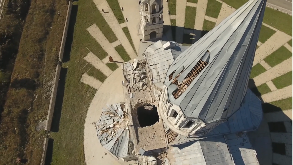 An aerial view looking down the damaged spire of a cathederal to a holes in the roof caused by shelling.