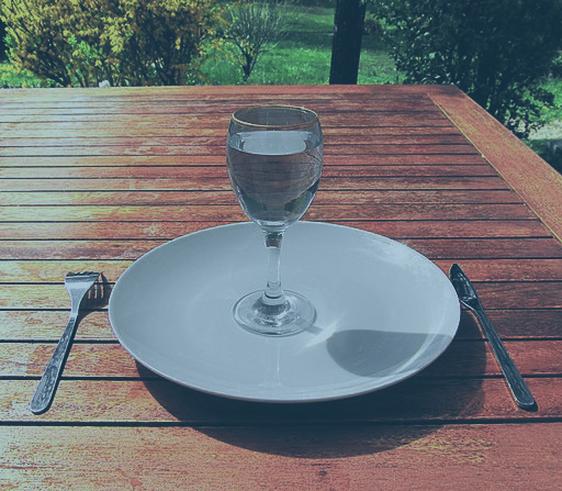 A wine glass of water sits on an empty clean plate.
