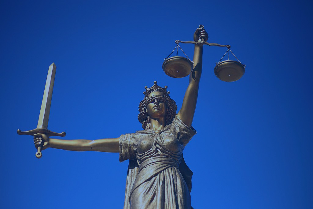 A statue of Justice holds a sword aloft in one hand, and set of scales in the other.