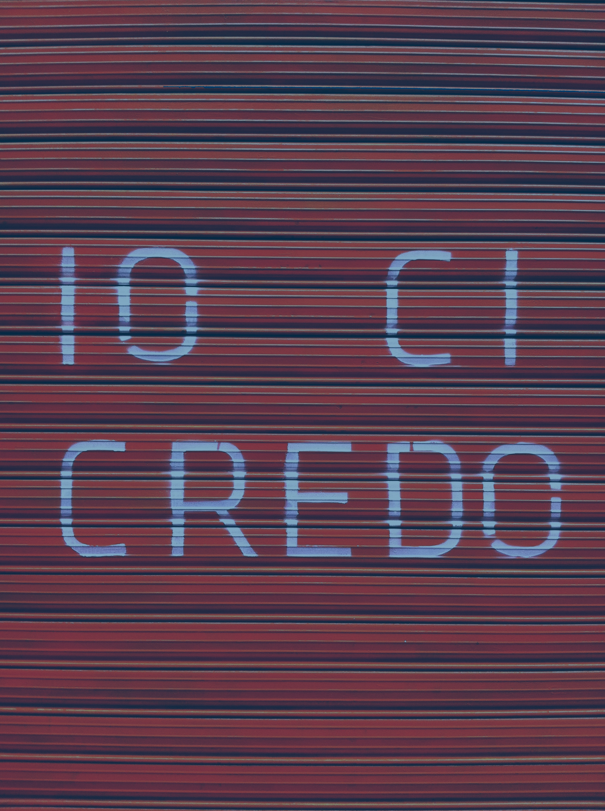 A red shutter door bears a large painted message reading 'io ci credo'