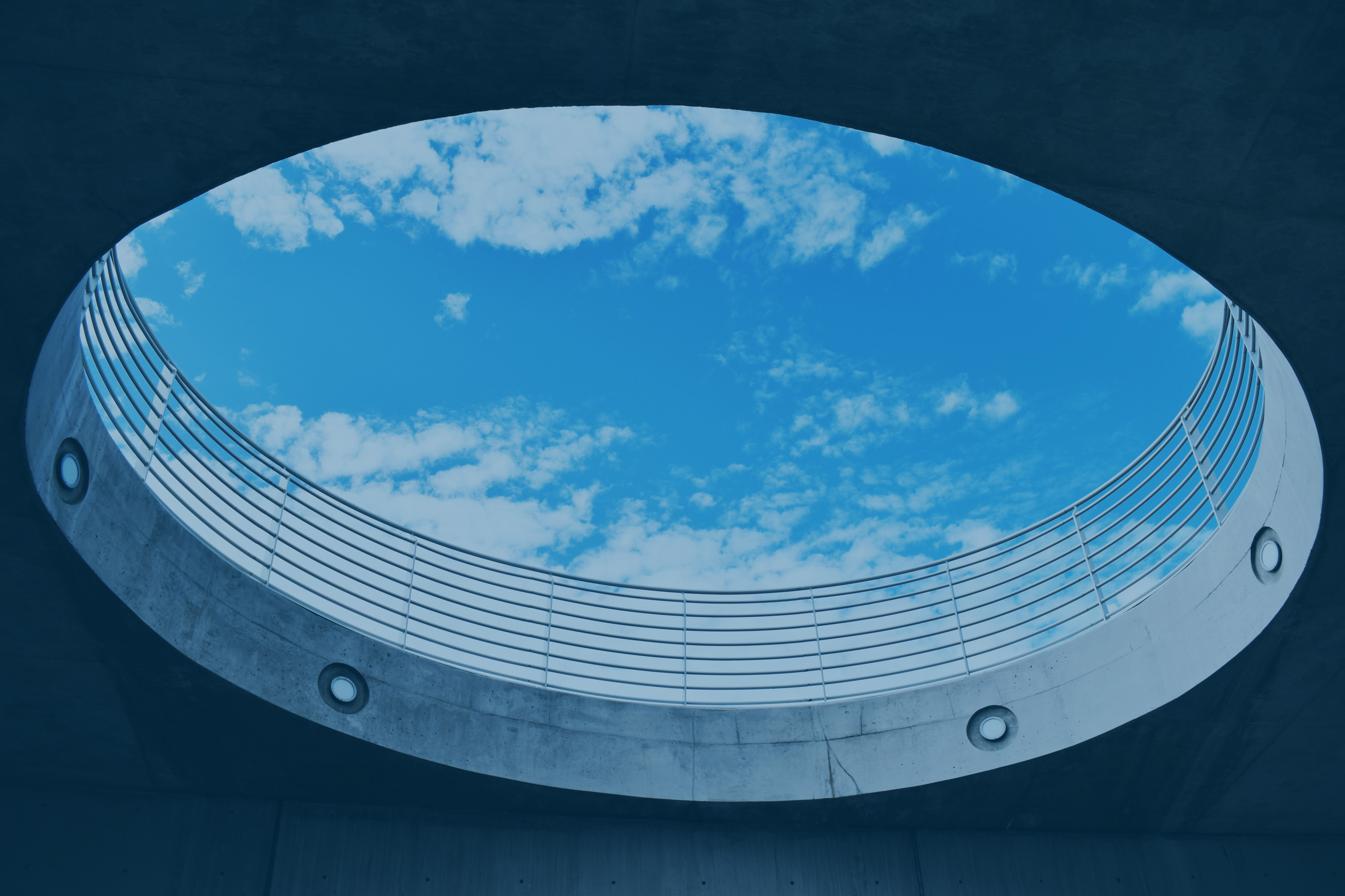 A cloud-dappled s blue sky is viewed through a large circular opening, from below.  