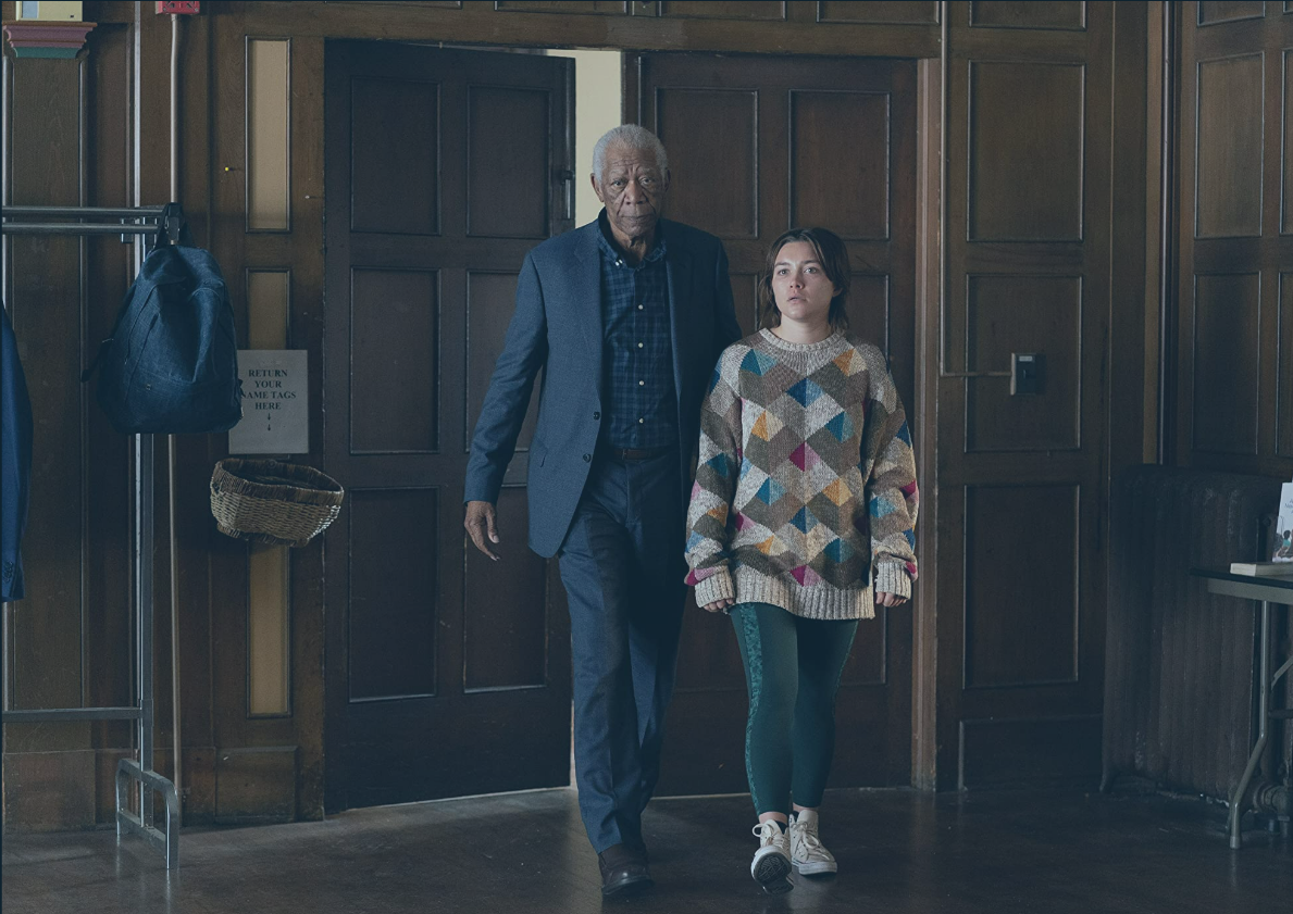 An old man accompanies a young woman into a wood-panelled hall, both look aprehensive.