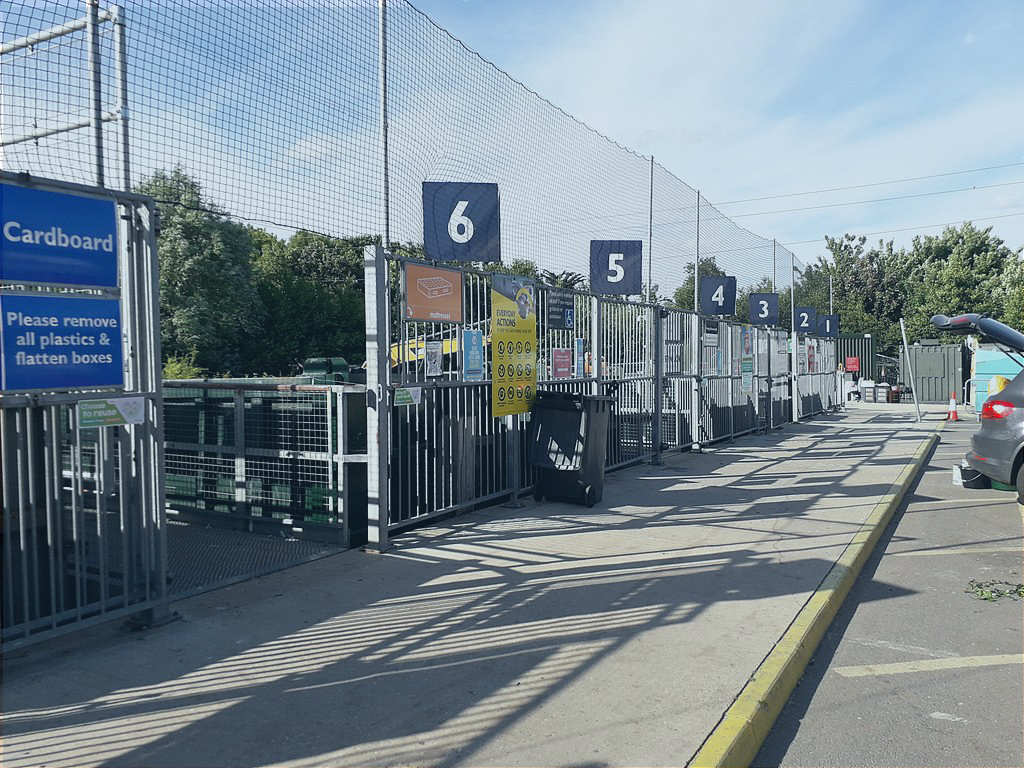 A recyling centre with numbered bays and high netting to catch wind-blown waste.