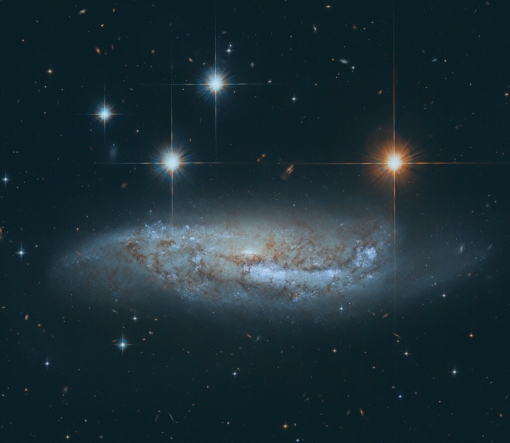 Four stars scintilate above a spiral galaxy viewed from the side.