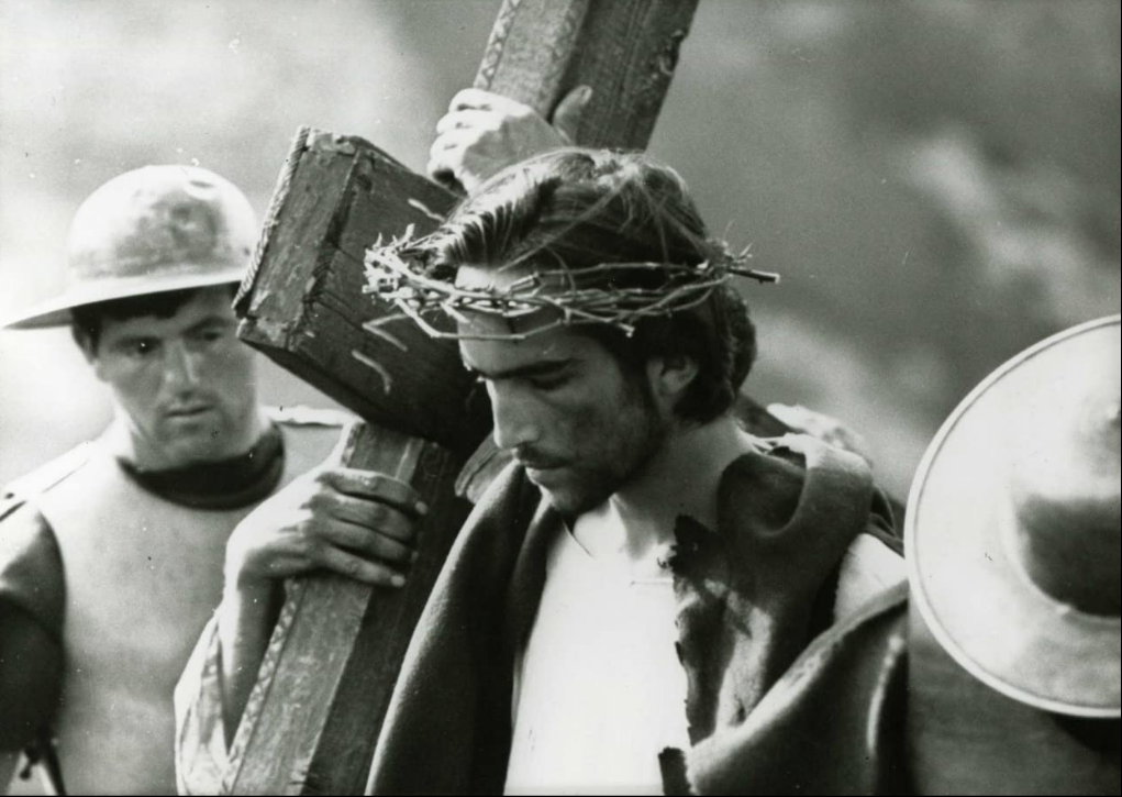 Jesus carries a cross over his shoulder while Roman soldiers wearing armour look on