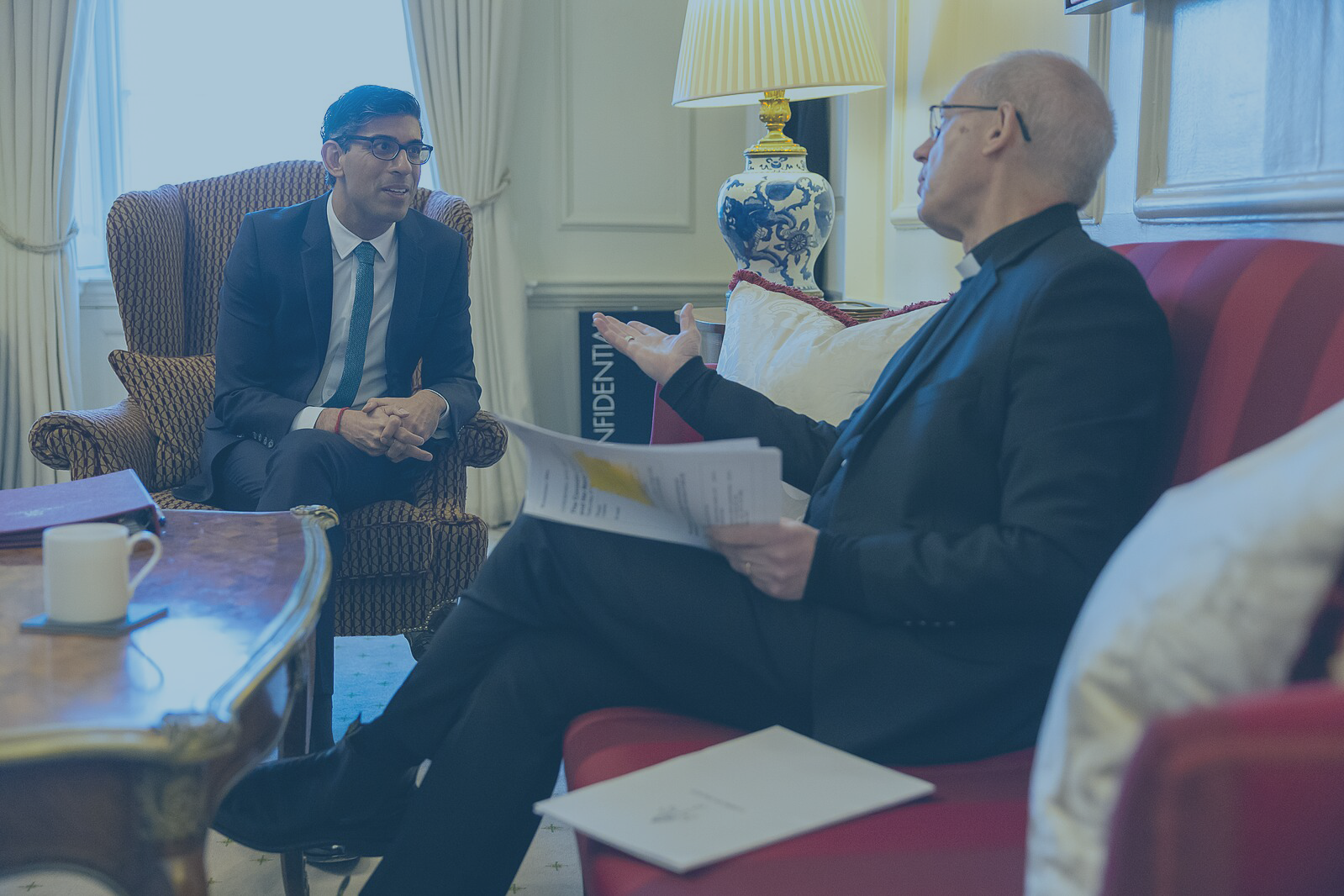 Prime minister Rishi Sunak leans forward out a lounge chair while the Archbishop of Canterbury talks and gestures while sitting on a sofa.