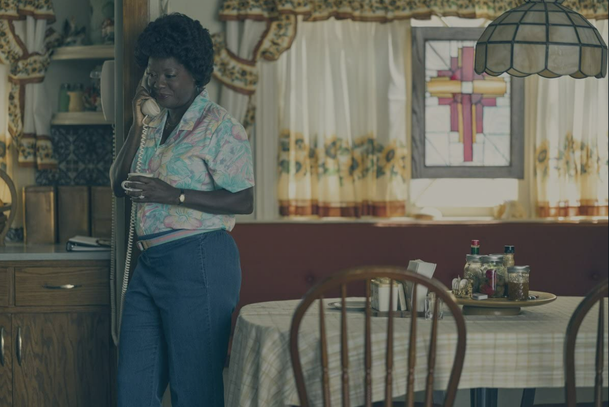 A woman stands in a kitchen diner hold a phone with a cord.