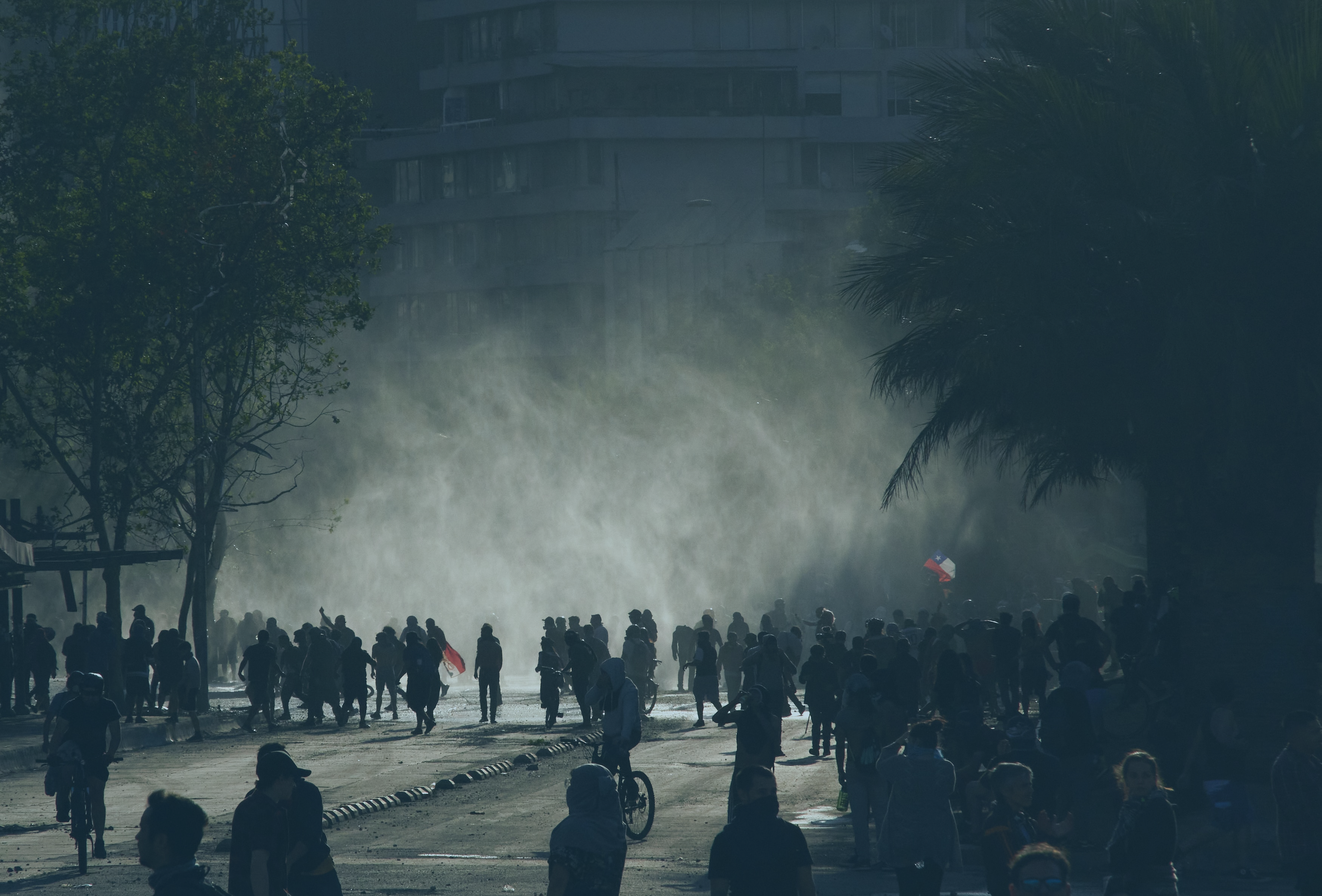 A loose rabble of a protest in the street is siluhetted against light and a shower of rain