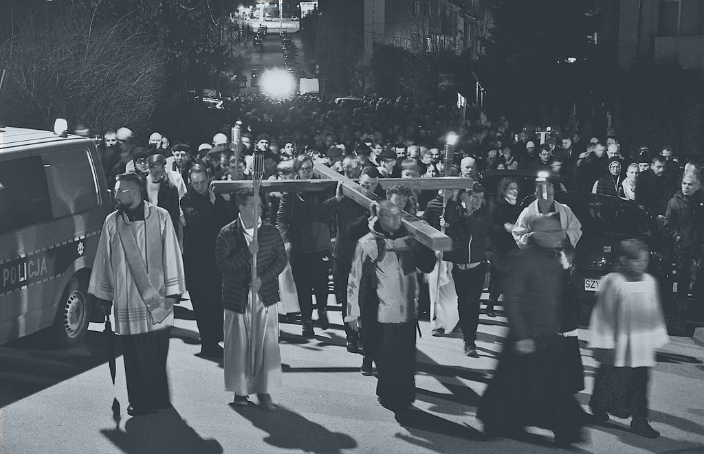 A Good Friday procession of people and priests hold a cross horizontal above their heads.