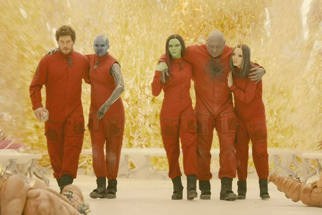 Five people in red jump suits help each other stand together.