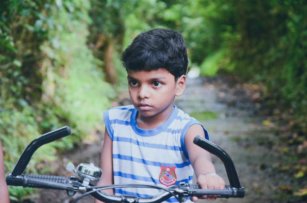 A child astride a stopped bicycle stares to the side.