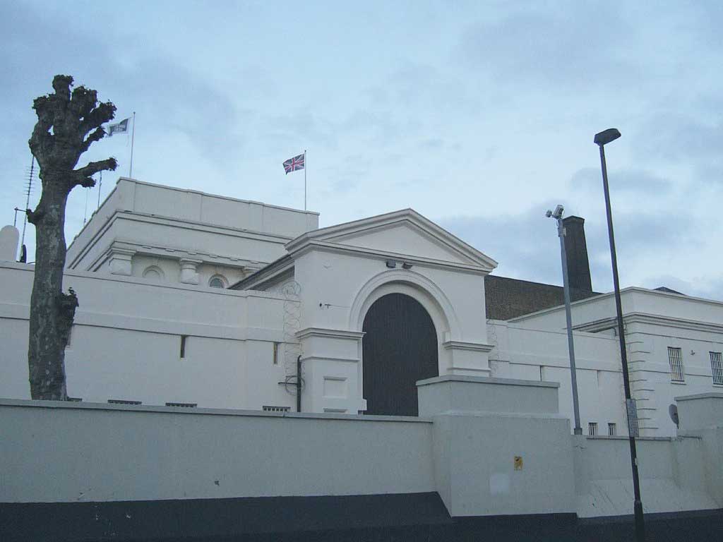 An arched gateway to a prison sits behind a low raised wall. No windows are visible