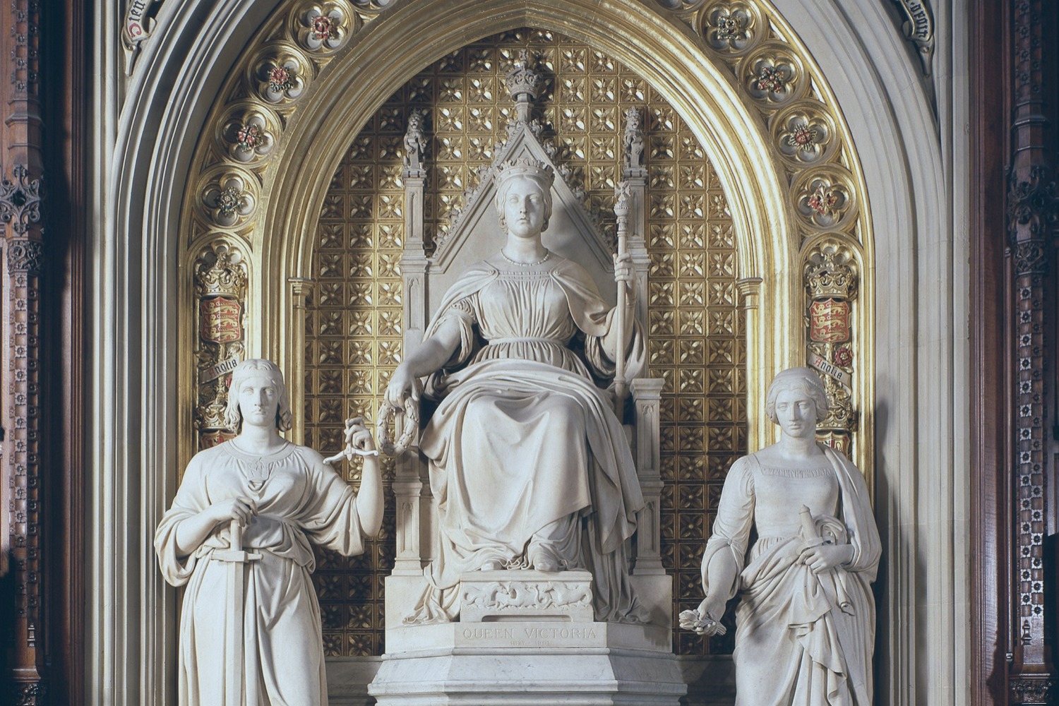 Under a gilded arch, a statue of a young Queen Victoria sits, between two standing figures.