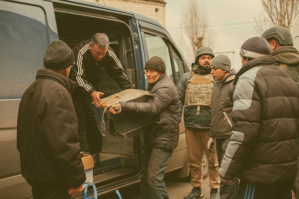 People help unload aid parcels from the side of a van, some wearing body armour.