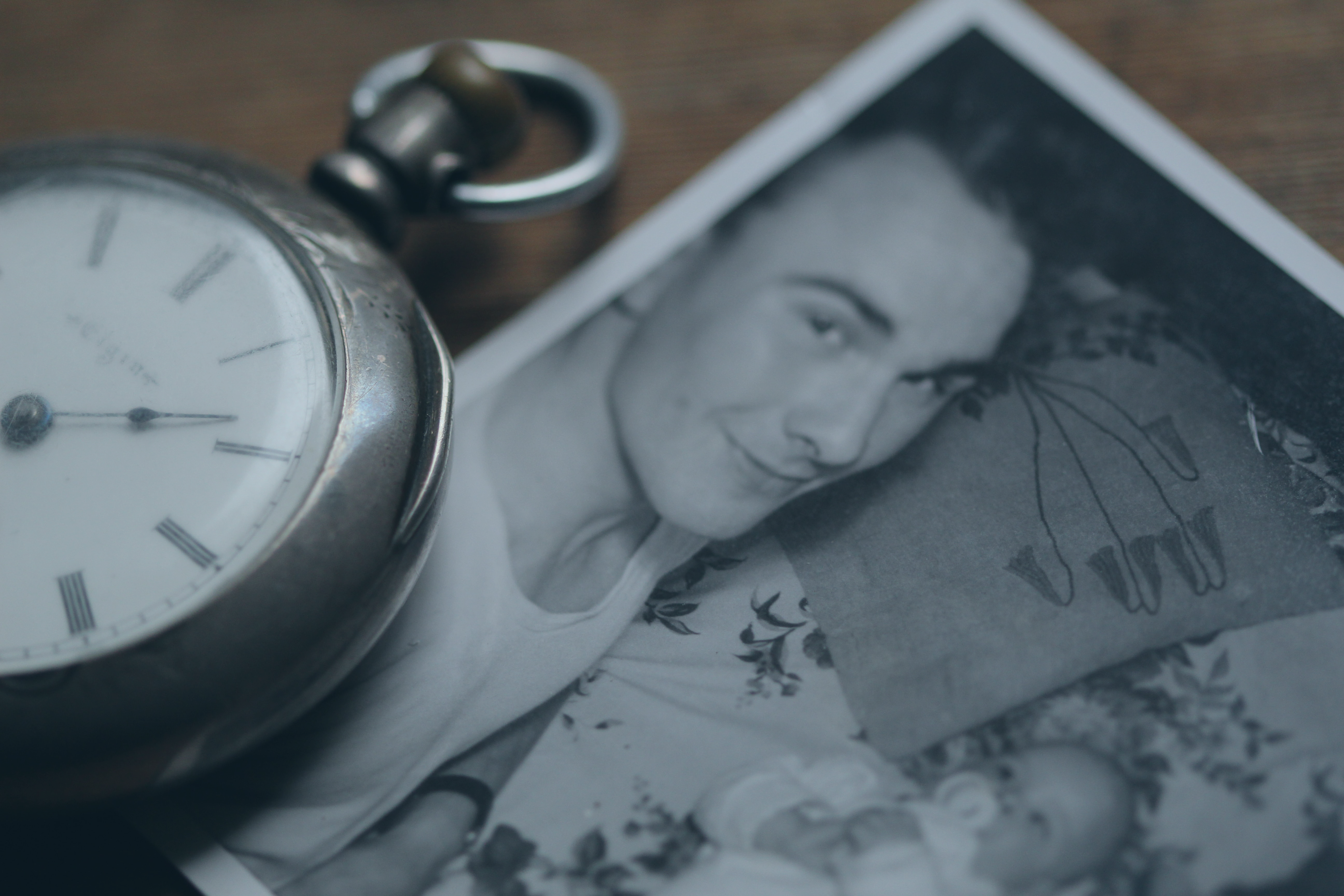 A pocket watch rests next to a black and white photograph of a father lying beside a new born baby.