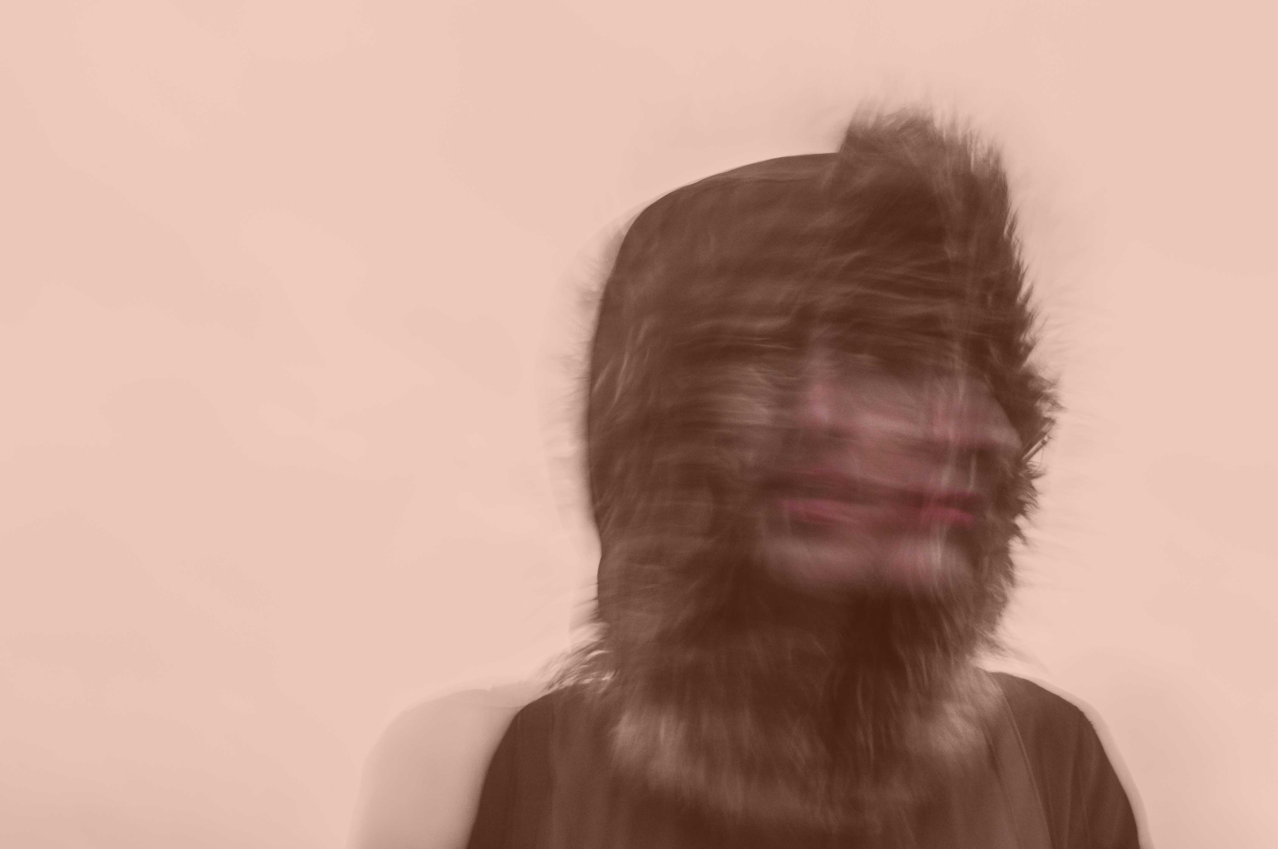 A blurred exposure of a person under a hood turning their head to the side.