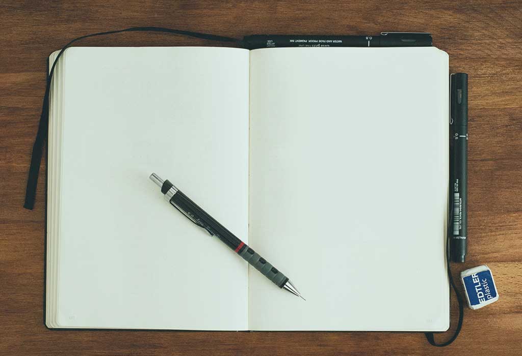 A notebook is open at two blank pages. a pen rests across the page.s.