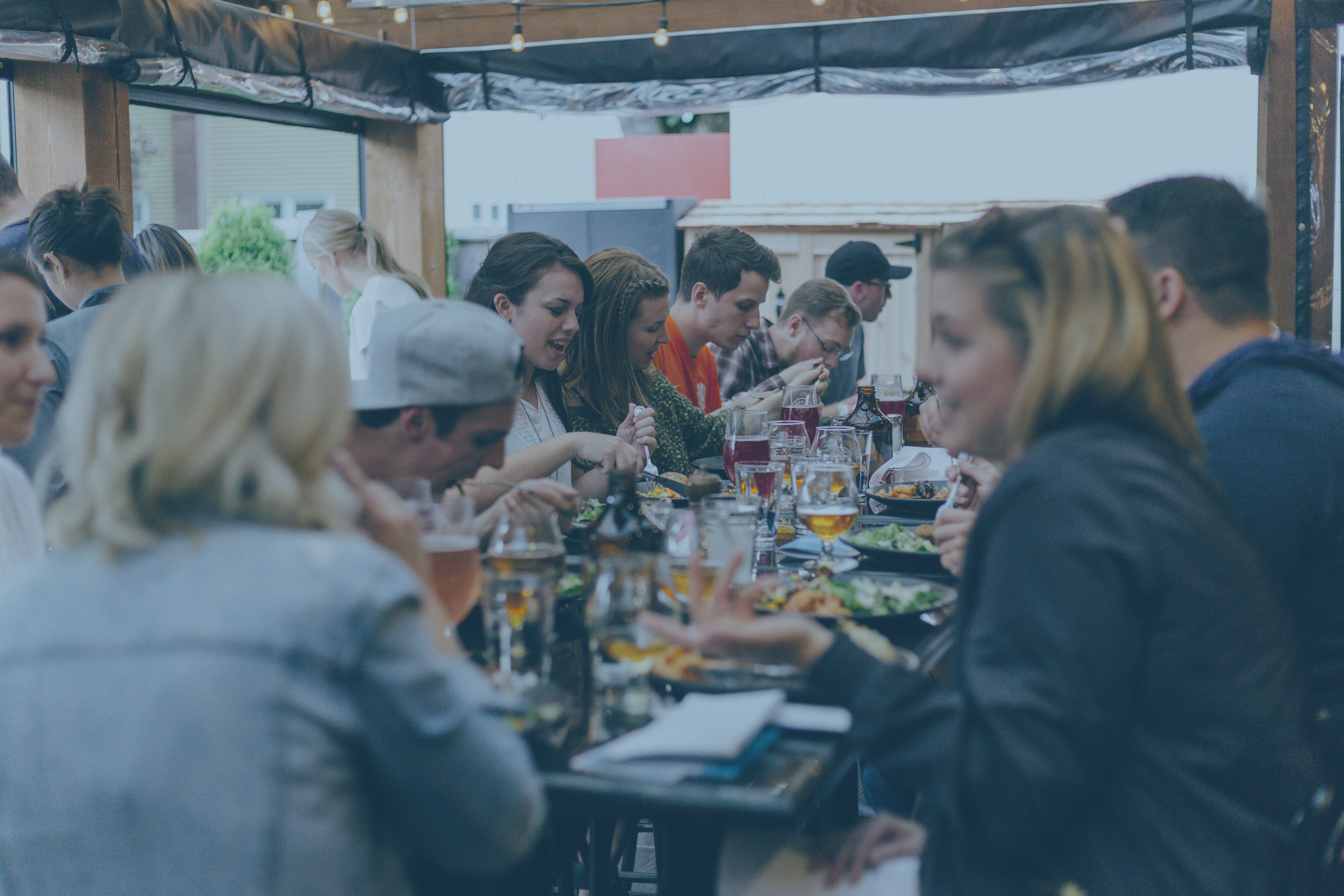 A large group of friends sit at a crowded table and share a meal together.