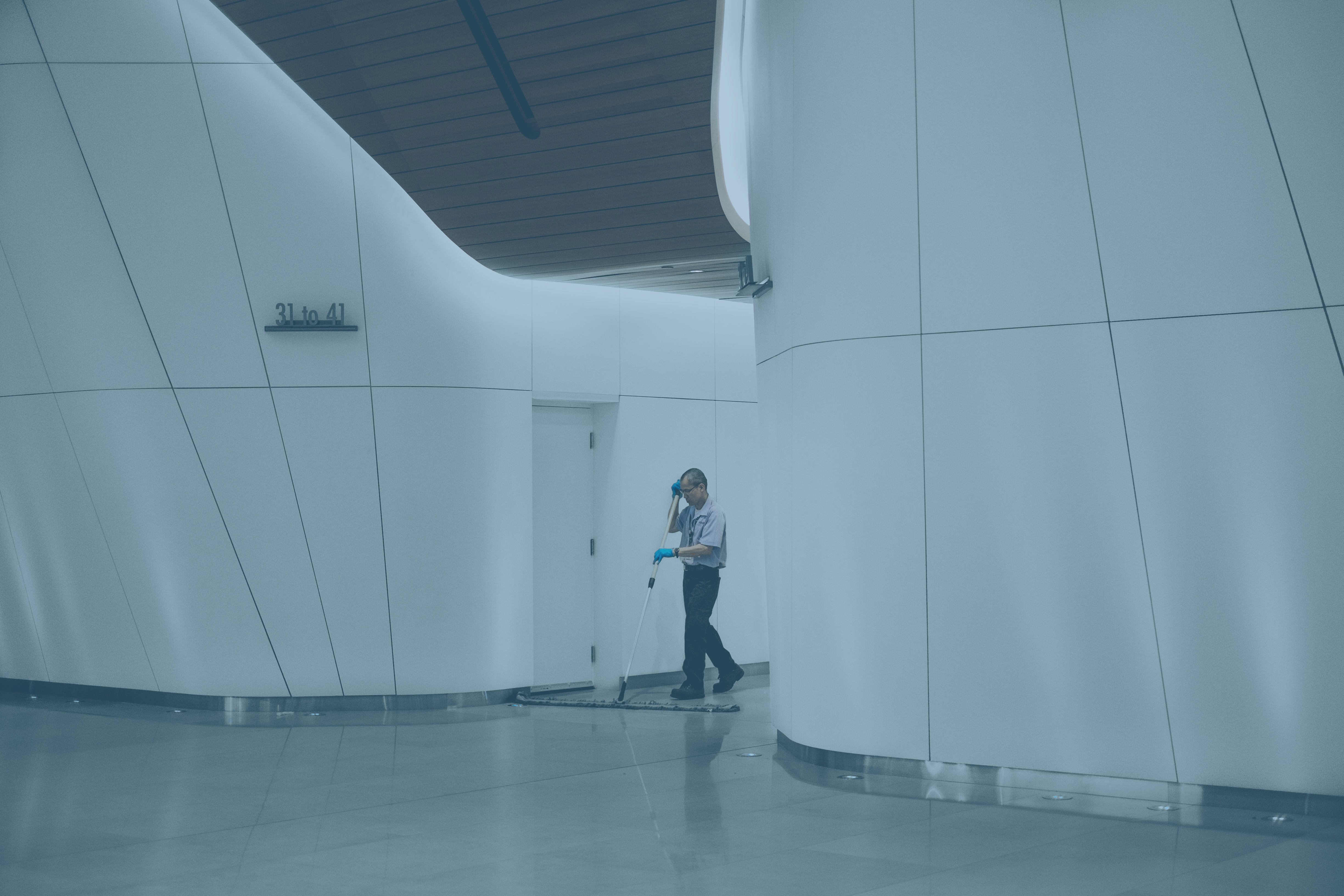 A cleaner sweeps between large white interior walls of a concourse.