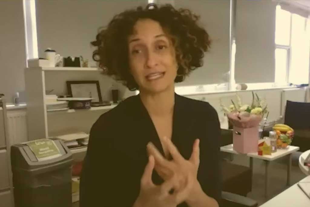 A head teacher sits at her desk, holding her hands in a gesture in front of her.