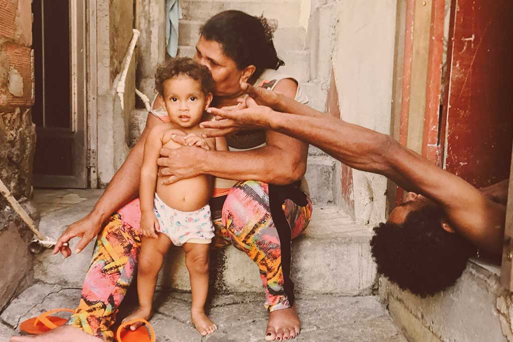 A mother sits with a toddler standing in front of her. The father appears from the side lying on his back reaching an arm out.