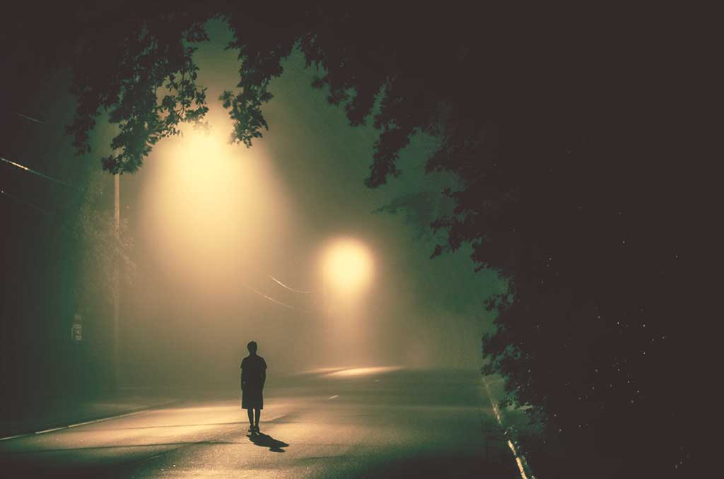A person stands in a road under misty street lights.