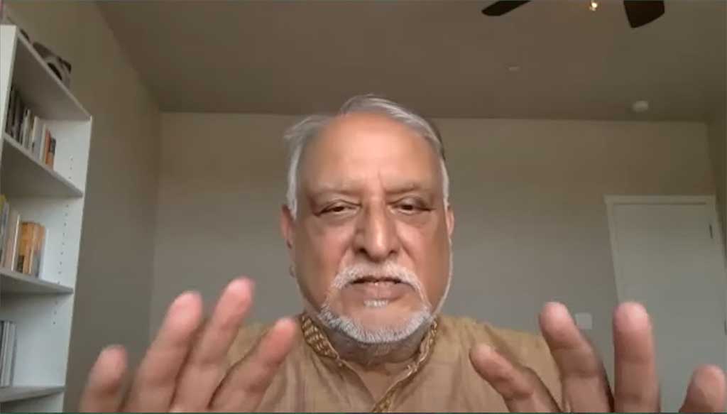 A man holds both hands up as he talks to a web cam