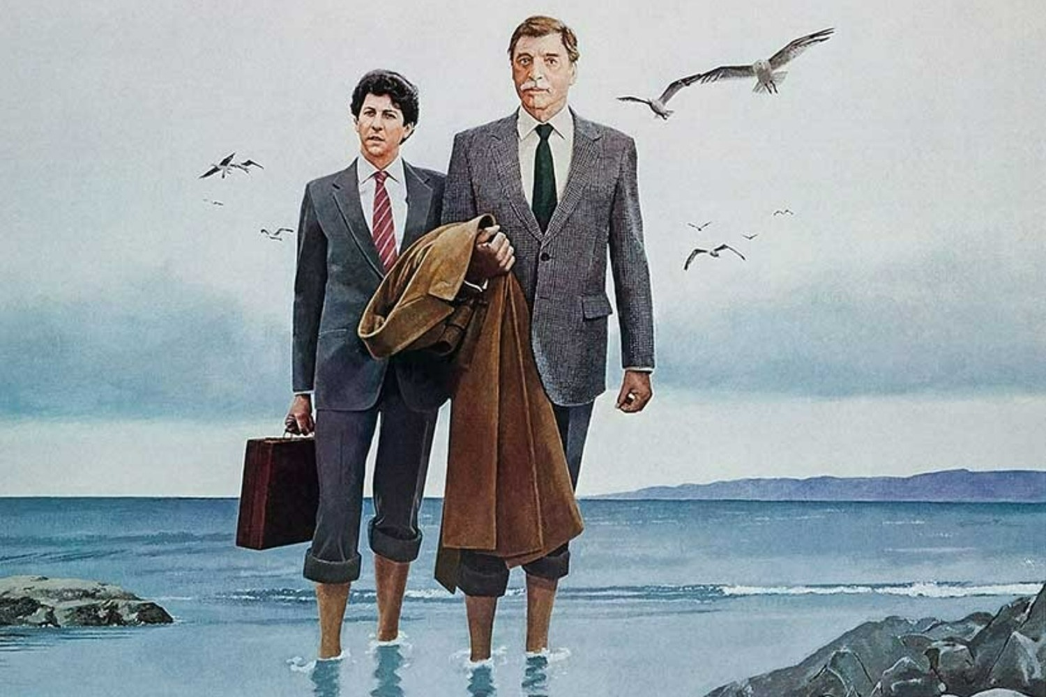 Two business men in suits hold coats and briefcases, stand in the sea with their trousers rolled-up above their ankles