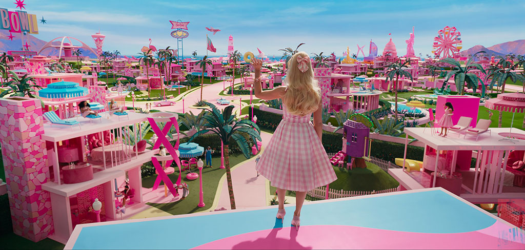 Barbie stands on a balcony and waves while looking out over her city.
