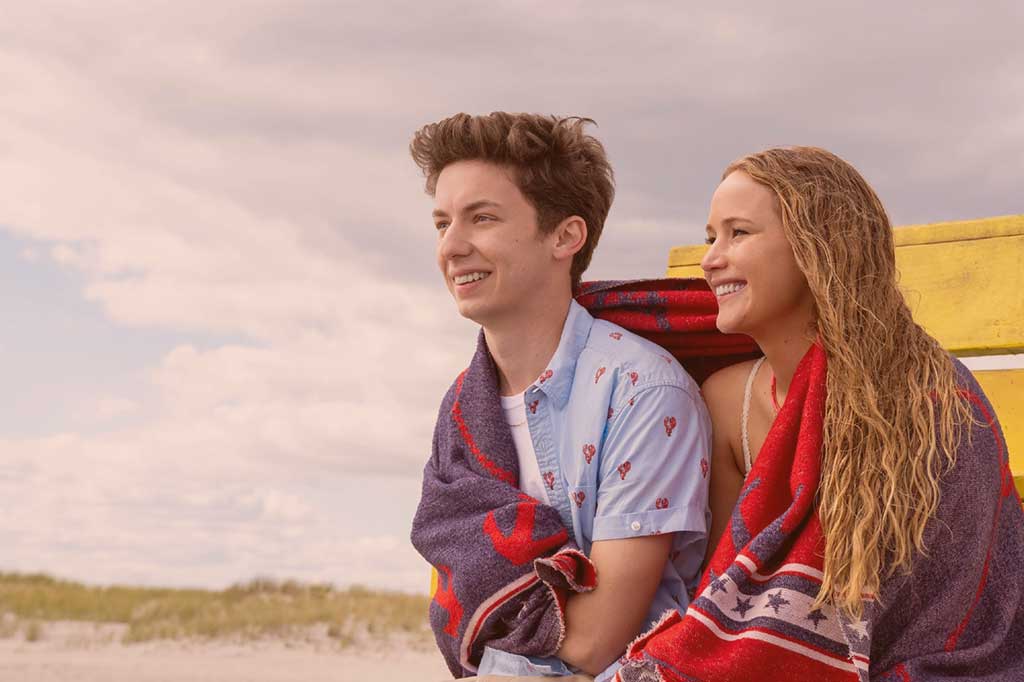 A young couple sit next to each other on a beach sharing a towel.