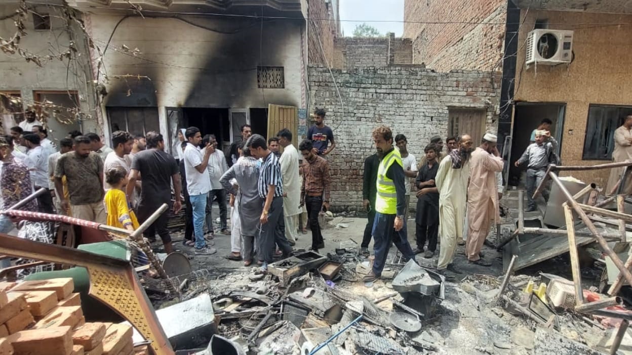 A crowd of people inspect fire damaged debris outside a burnt-out church.