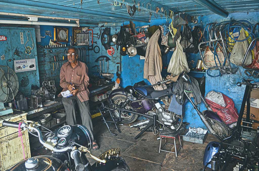 A mechanic stands in a workshop beside a motorcycle under repair.