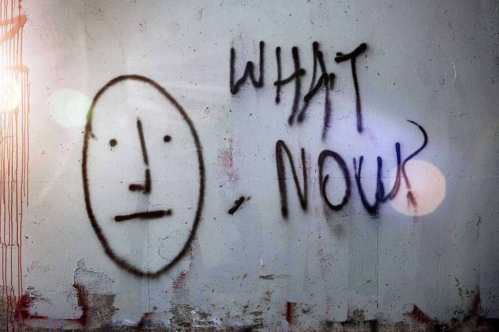 A graffited wall shows a stick man face next to 'what now'