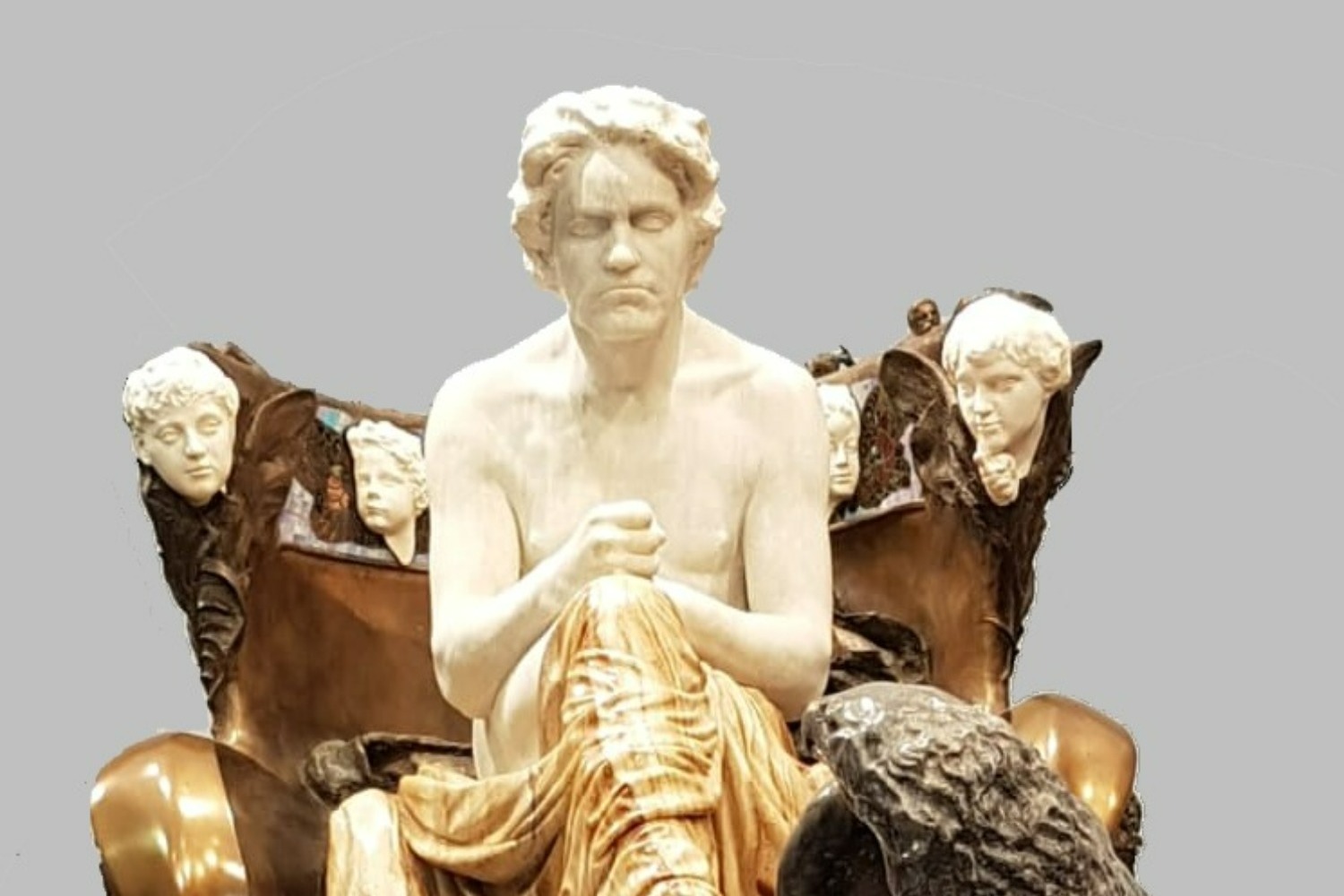Agrand statue of Beethoven as a classical hero seats him on a throne on a dias.