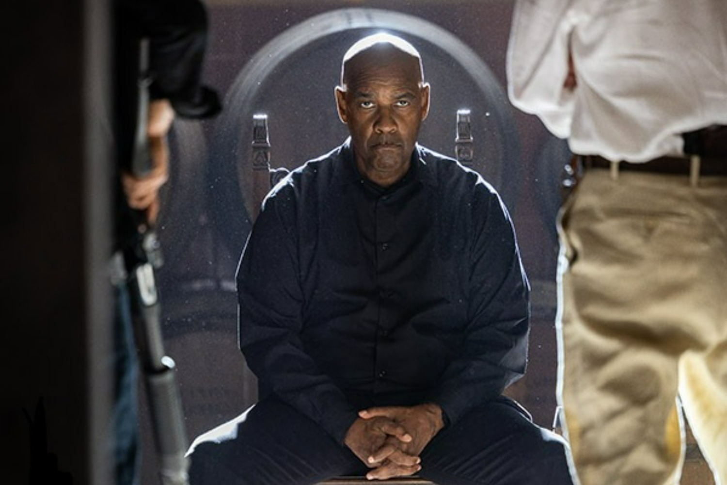 A serious looking man in black sits pensively on a carved chair.