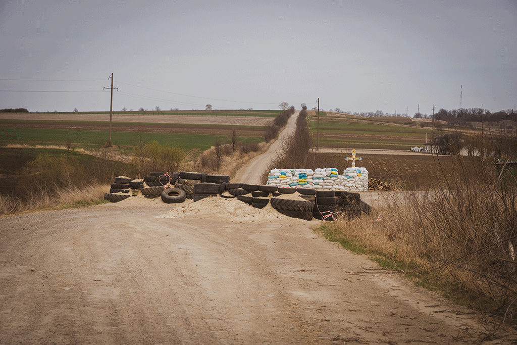 a dirt barricade blocks a cross roads, behind which stands a roadside cross