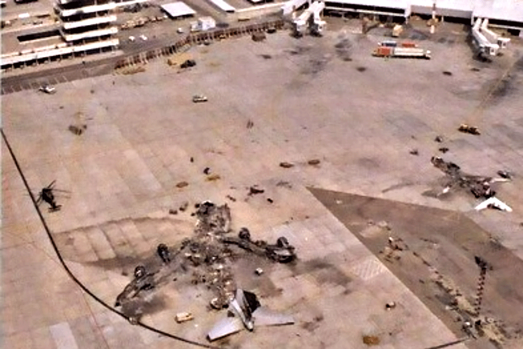 A destroyed airliner lies on the apron of a war-torn airport.