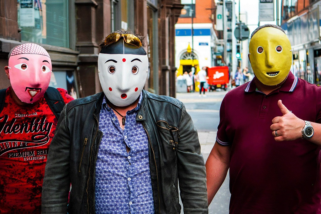 Three men wearing pink, spotty and yellow face masks stand in the street.