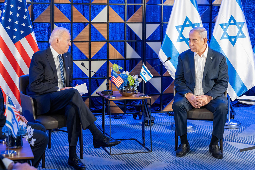 Two country leaders sit in chairs next to each other with their country's flags behind