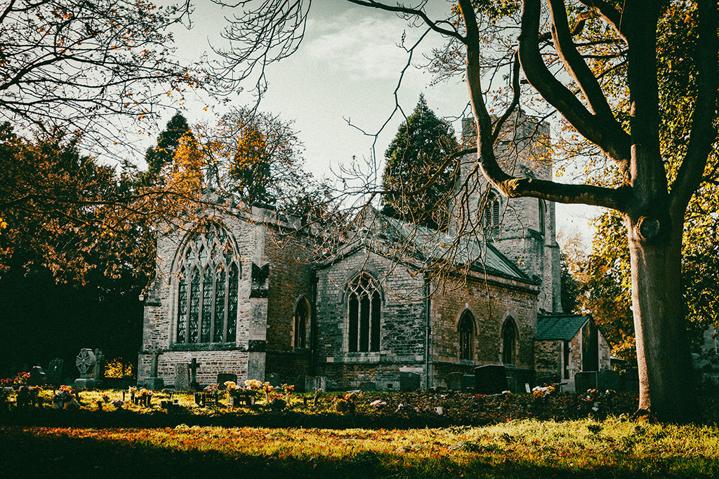 An autumnal scene of a church yard and church framed by leafless trees.