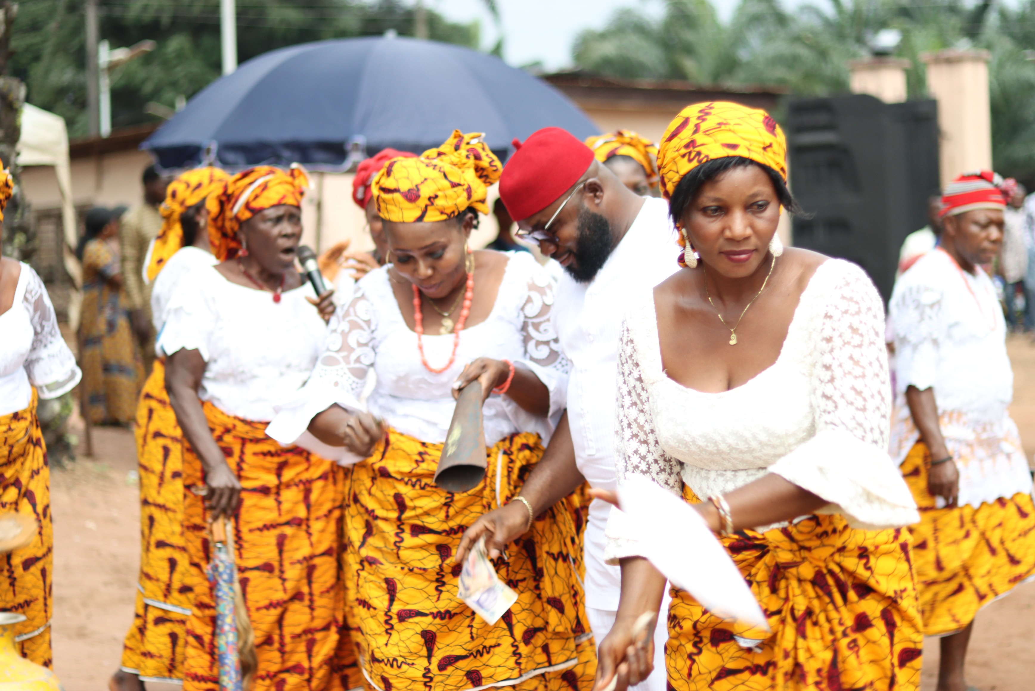 A group of women stand and dance at a celebration in the street, wearing matching skirts..