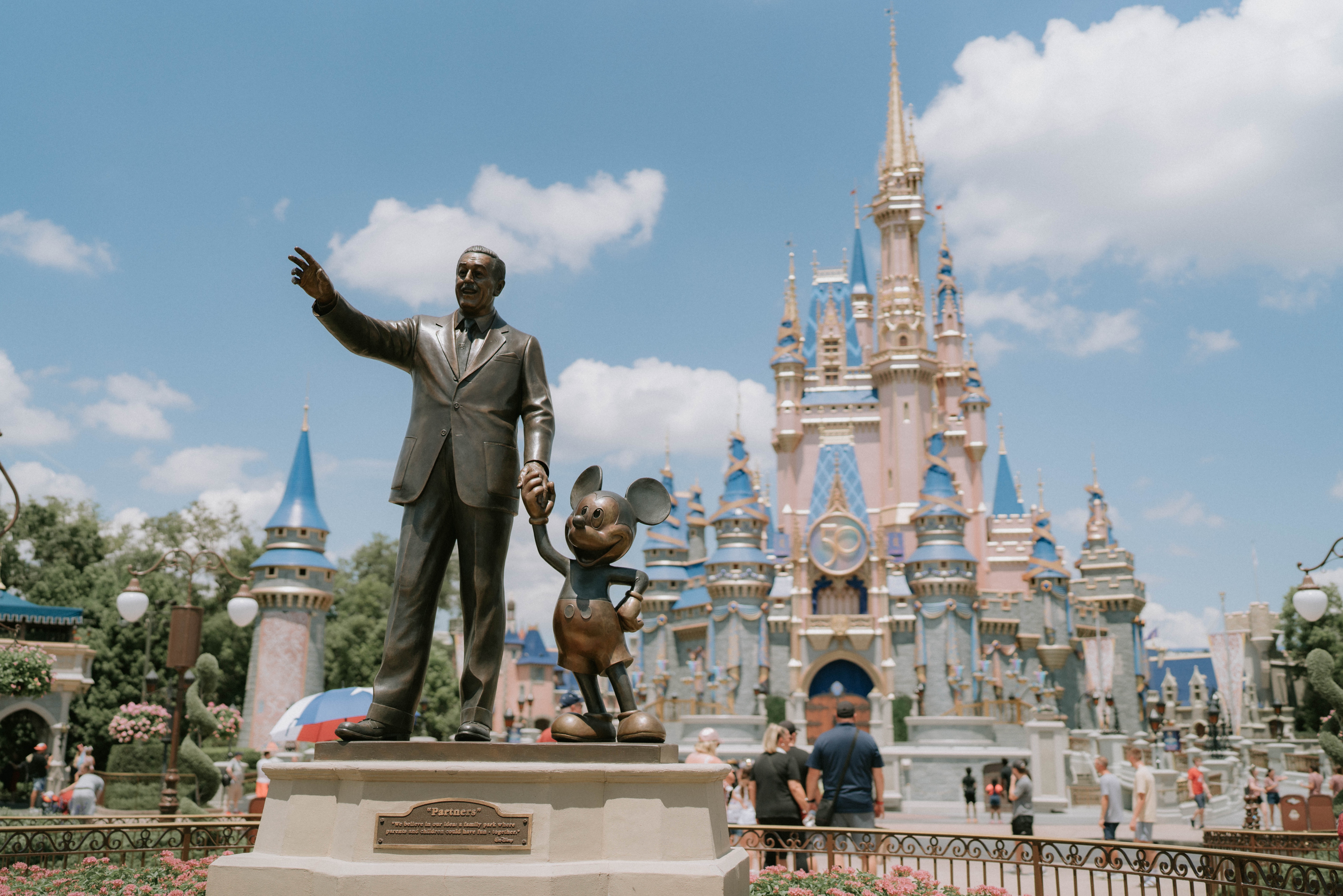 A statue of Walt Disney holding hands with Mickey Mouse in front of Cinderella's Castle
